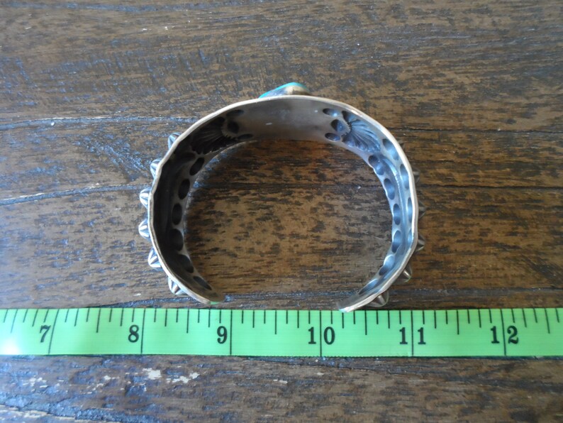 K&ouml;nnte beinhalten: Silberarmband mit T&uuml;rkis-Stein-Einlage und dekorativen Details. Das Armband hat einen Durchmesser von etwa 23 cm.