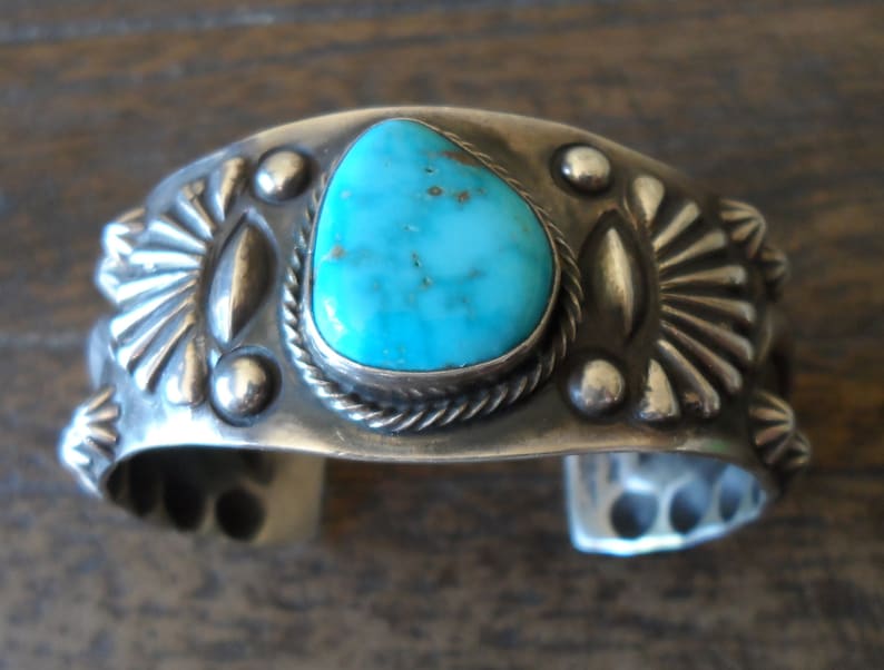 K&ouml;nnte beinhalten: Ein silbernes Armreif mit einem T&uuml;rkis-Stein in der Mitte. Das Armband ist mit silbernen Perlen und geometrischen Mustern verziert.