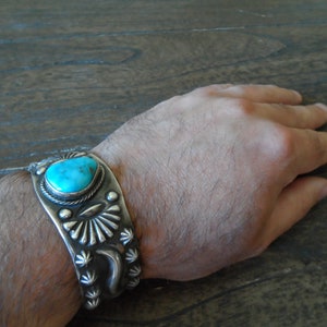 K&ouml;nnte beinhalten: Ein silbernes Armband mit einem t&uuml;rkisfarbenen Stein in der Mitte. Das Armband ist mit komplizierten Silberdesigns verziert.
