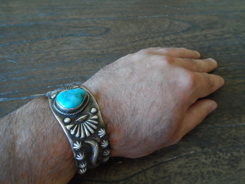 K&ouml;nnte beinhalten: Ein silbernes Armband mit einem t&uuml;rkisfarbenen Stein in der Mitte. Das Armband ist mit komplizierten Silberdesigns verziert.