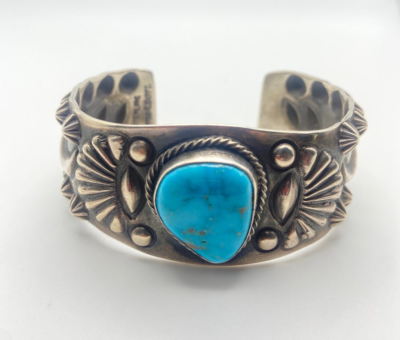K&ouml;nnte beinhalten: Ein silbernes Armreif mit einem T&uuml;rkis-Stein in der Mitte. Das Armband ist mit komplizierten Silberdesigns verziert.