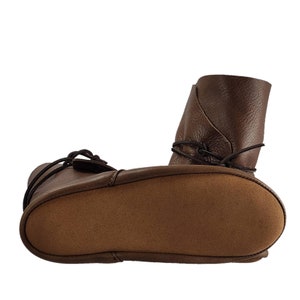 K&ouml;nnte beinhalten: Braune Lederstiefel im Mokassin-Stil mit Wildledersohle und Schn&uuml;rsenkeln. Die Stiefel sind umgeklappt, um die Sohle zu zeigen.