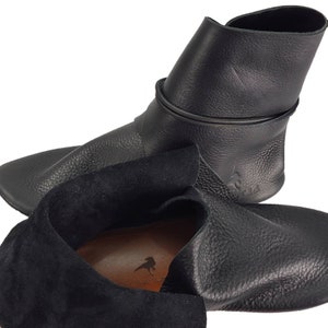 K&ouml;nnte beinhalten: Ein Paar schwarze Lederstiefel mit Kn&ouml;chelh&ouml;he, einem umgeschlagenen Oberteil und einem Futter aus Wildleder. Die Stiefel haben eine spitze Zehenpartie und eine flache Sohle.
