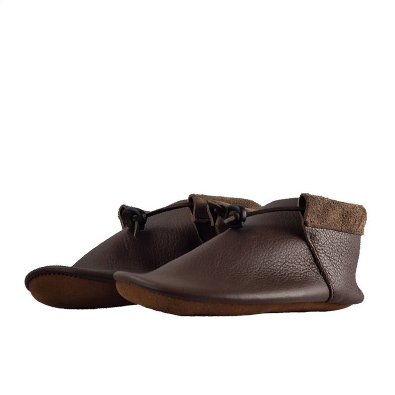 May include: A pair of brown leather moccasins with a suede trim and a black leather tie closure.