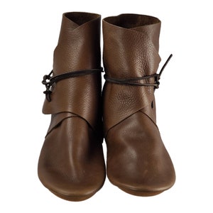 K&ouml;nnte beinhalten: Ein Paar braune Lederstiefel mit Schnallen, die sich um den Kn&ouml;chel wickeln. Die Stiefel haben eine spitze Zehenpartie und einen niedrigen Absatz.