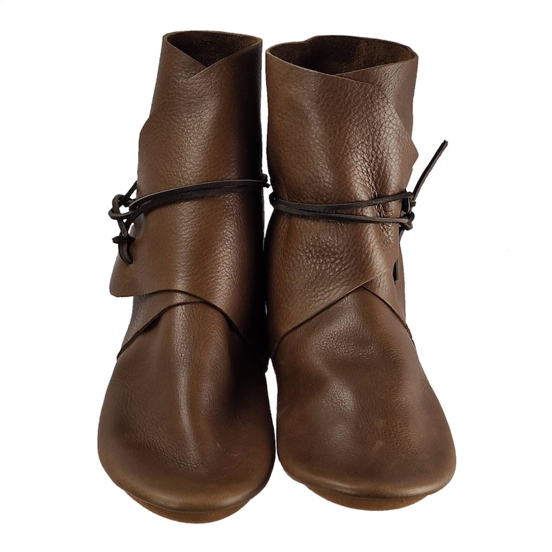 K&ouml;nnte beinhalten: Ein Paar braune Lederstiefel mit Schnallen, die sich um den Kn&ouml;chel wickeln. Die Stiefel haben eine spitze Zehenpartie und einen niedrigen Absatz.
