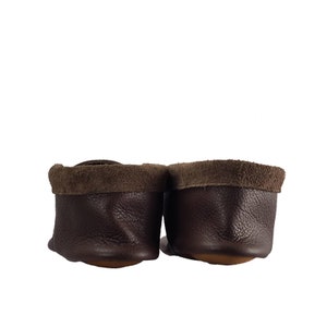 May include: A pair of brown leather moccasins with suede trim. The moccasins are shown from the back, with the soles facing the viewer.