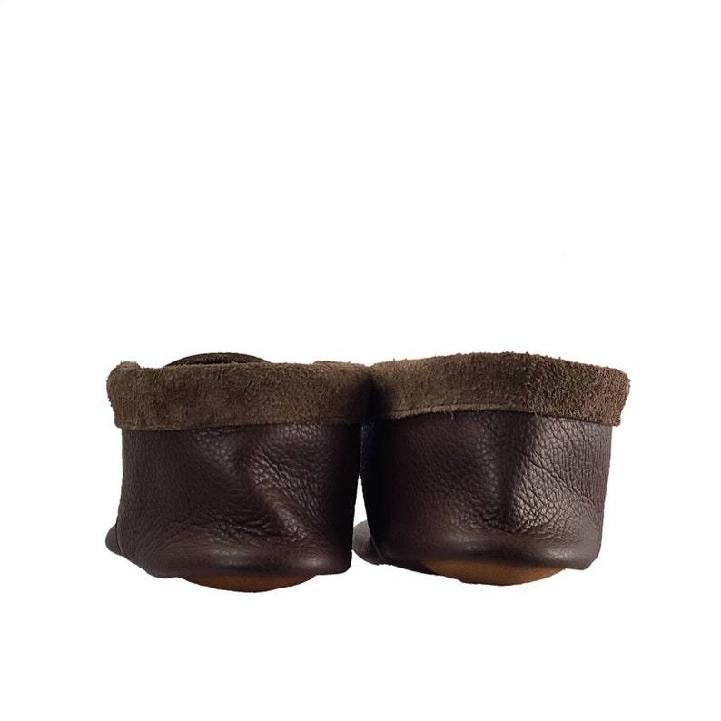 May include: A pair of brown leather moccasins with suede trim. The moccasins are shown from the back, with the soles facing the viewer.