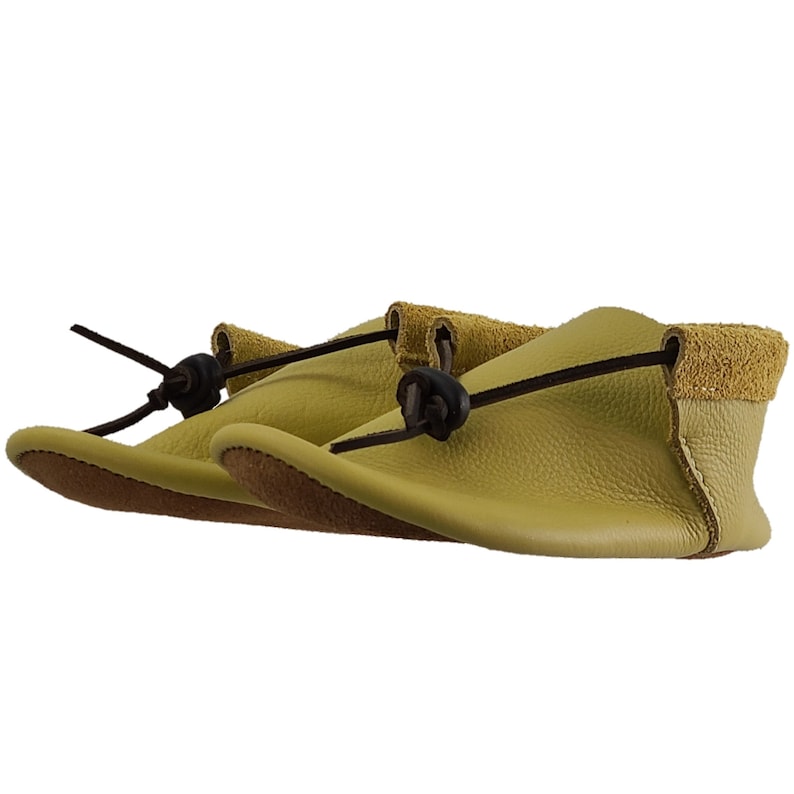 May include: A pair of light green leather moccasins with brown leather laces and ties. The moccasins have a suede trim around the top.
