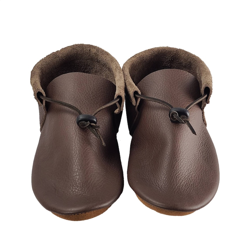 May include: A pair of brown leather moccasins with a fold-over cuff and a tie closure. The moccasins have a textured leather surface and a rounded toe.