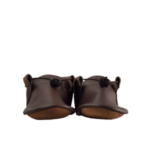 May include: A pair of brown leather moccasins with a simple design and a tie at the top.