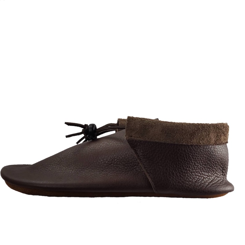 May include: Brown leather moccasin with a suede cuff and a leather tassel. The moccasin has a flat sole and a rounded toe.