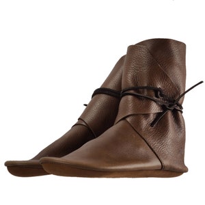 K&ouml;nnte beinhalten: Ein Paar braune Lederstiefel mit einem umgeschlagenen Oberteil und einem Schn&uuml;rverschluss. Die Stiefel haben eine flache Sohle.