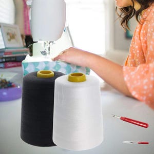 May include: Two spools of thread, one black and one white, are sitting on a table. A sewing machine is in the background.