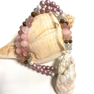 May include: A multi-strand bracelet with pink, green, and white beads. The bracelet is wrapped around a seashell.