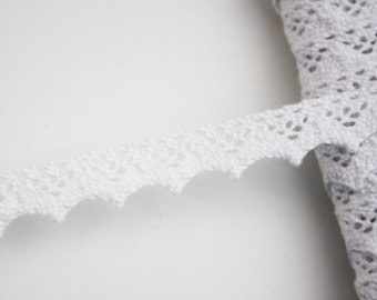 May include: White crochet trim with a scalloped edge. The trim is delicate and intricate, with a floral pattern.