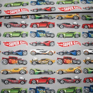 Könnte beinhalten: Grauer Stoff mit einem sich wiederholenden Muster aus bunten Spielzeugautos in verschiedenen Designs. Die Autos sind rot, grün, blau, gelb und weiß, mit Flammen und anderen Grafiken. Die Worte "SUPER Cars" erscheinen in einem roten Banner.