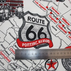 May include: A white fabric with a black and white Route 66 sign with the text "PONTIAC. III INOIS". The sign is on a map of the United States with red dots marking the route of Route 66. A ruler is placed on the fabric.