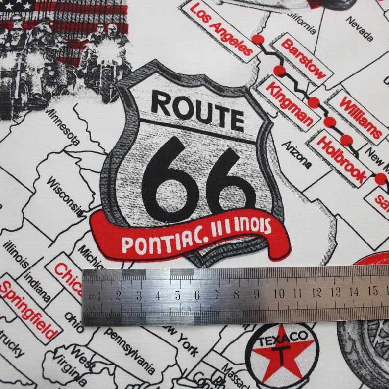 May include: A white fabric with a black and white Route 66 sign with the text "PONTIAC. III INOIS". The sign is on a map of the United States with red dots marking the route of Route 66. A ruler is placed on the fabric.