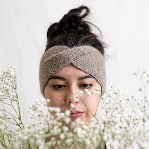 May include: A woman with dark hair wearing a brown knitted headband looks down at a bouquet of white baby's breath flowers.