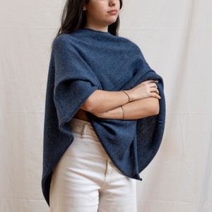 Könnte beinhalten: Ein blauer Strickponcho mit einem Rollkragen. Der Poncho ist aus einem weichen, bequemen Stoff gefertigt und hat eine lockere Passform.