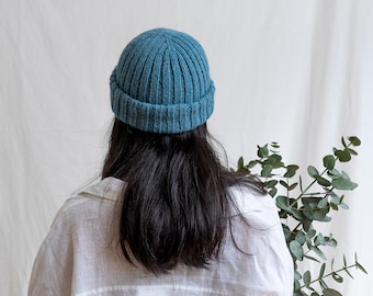 Puede incluir: Una persona con un gorro de punto azul turquesa y una camisa blanca. La persona tiene el pelo largo y negro y está de espaldas a la cámara.