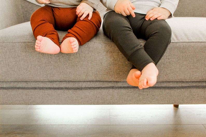 Pode incluir: Duas crian&ccedil;as pequenas sentadas em um sof&aacute; cinza vestindo leggings marrons e cinza.