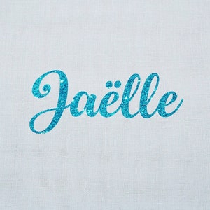 May include: A light blue fabric with the name "Jaëlle" in a glittery, cursive font. The name is centered on the fabric. The lower right corner features a logo with the text "Flex Sandelisabeth" and a butterfly.