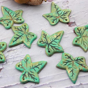 Op de afbeelding: Acht blad-vormige decoratieve kralen in turquoise met gouden accenten en zwarte aderen. Elke kraal heeft twee kleine gaatjes om te rijgen. Perfect voor knutselprojecten.