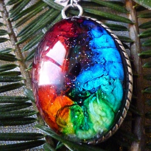 May include: A colorful, iridescent pendant with a silver chain and bow. The pendant is round and features a swirling pattern of red, orange, yellow, green, blue, and black.