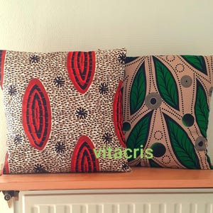 May include: Two decorative throw pillows with geometric patterns. One pillow has a beige background with red and black oval shapes. The other pillow has a beige background with green leaf shapes and black circles.