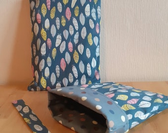 Puede incluir: Dos bolsas de tela azul turquesa con un patrón de plumas de colores. Una bolsa está abierta y muestra un forro de lunares azul turquesa y blanco. Las bolsas están sobre una superficie de madera.