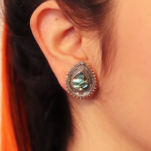 May include: A pair of silver teardrop-shaped earrings with a green abalone shell inlay. The earrings have a detailed, ornate design.
