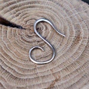 May include: Silver S-shaped earring with a curled end. The earring is on a wooden surface.
