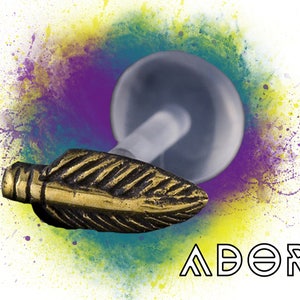 May include: A gold-colored feather-shaped body jewelry piece with a clear acrylic ball on the end. The jewelry is set against a colorful background with the word "ADORE" in white text.