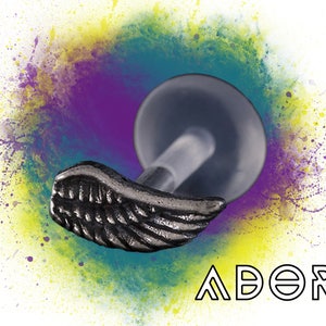 May include: A silver-colored wing-shaped stud earring with a clear post and a flat, round backing. The word "ADORE" is written in outlined capital letters below the earring. The background features a colorful splash of purple, yellow, and teal.
