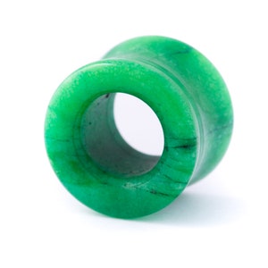 May include: A green jade stone ear gauge, also known as a flesh tunnel, with a smooth, polished finish. The gauge is a circular shape with a hole in the centre.