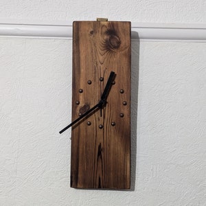 May include: A rustic wooden clock with black hands and metal accents. The clock face is made of reclaimed wood and has a distressed finish.