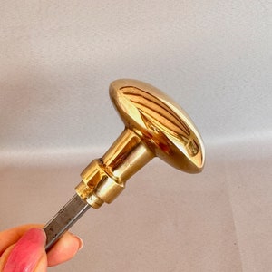 May include: A gold-toned door knob with a round, oval-shaped handle and a long, thin, silver-colored shaft.