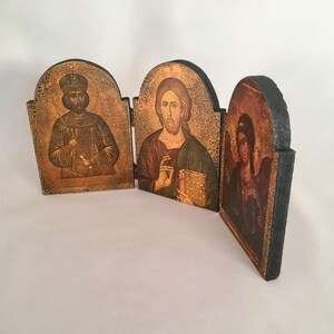 May include: A wooden triptych icon with three panels. The left panel features a man with a crown and beard, the middle panel features a man with a beard and a book, and the right panel features a woman with a halo and wings.