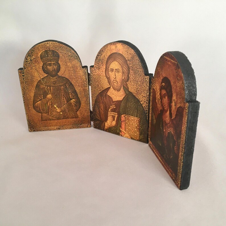 May include: A wooden triptych icon with three panels. The left panel features a man with a crown and beard, the middle panel features a man with a beard and a book, and the right panel features a woman with a halo and wings.