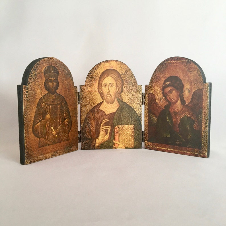 May include: A wooden triptych with three panels, each featuring a religious icon. The left panel depicts a man with a beard and a crown, the middle panel shows a man with a beard and a book, and the right panel shows a person with wings and a halo.