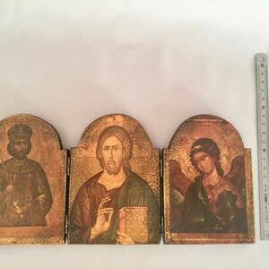 May include: A wooden triptych icon with three panels. The left panel features a man in a crown and robe, the middle panel features a man with a beard and a book, and the right panel features a winged angel with a halo.