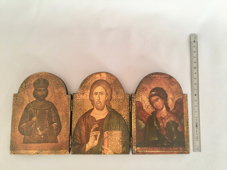 May include: A wooden triptych icon with three panels. The left panel features a man in a crown and robe, the middle panel features a man with a beard and a book, and the right panel features a winged angel with a halo.