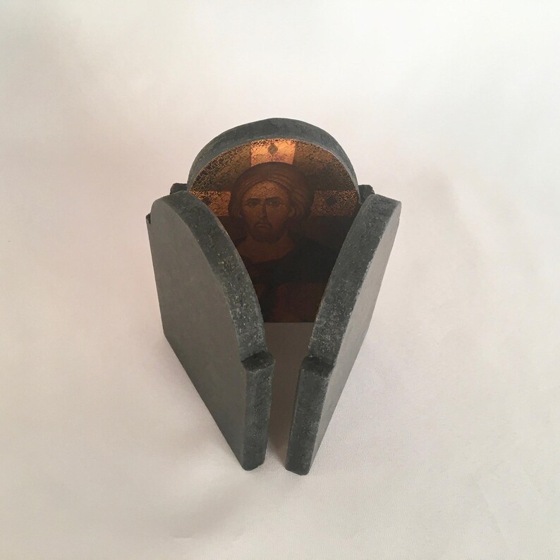 May include: A small, gray, stone-like box with a hinged lid. The lid is open, revealing a gold-colored image of Jesus inside.