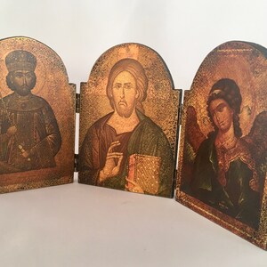 May include: A wooden triptych with three painted panels depicting religious figures. The center panel shows Jesus holding a book, the left panel shows a figure in a crown and robe, and the right panel shows an angel with wings.