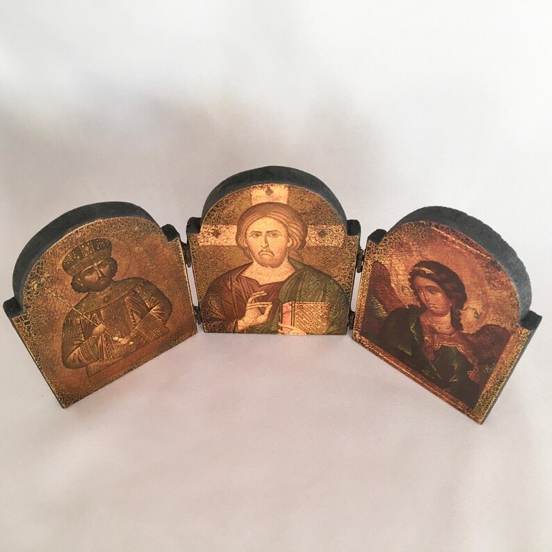 May include: A three-panel wooden icon set with gold-toned images of Jesus, a king, and an angel. The panels are hinged and can be folded together.