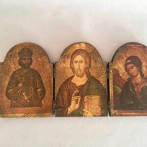 May include: A three-panel wooden icon set with gold accents. The center panel features a painting of Jesus Christ, while the left and right panels depict a king and an angel, respectively.