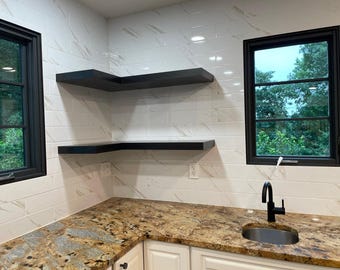 May include: A kitchen with white subway tile backsplash and black floating shelves. The countertop is a brown granite with a sink and black faucet. There are two windows with black frames.