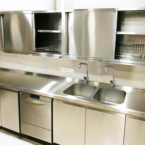 May include: A stainless steel kitchen with a double sink, a dishwasher, and wall-mounted cabinets with sliding doors. The cabinets have shelves and a dish rack.